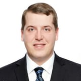 Headshot of a man in a black suit and blue tie against a white background